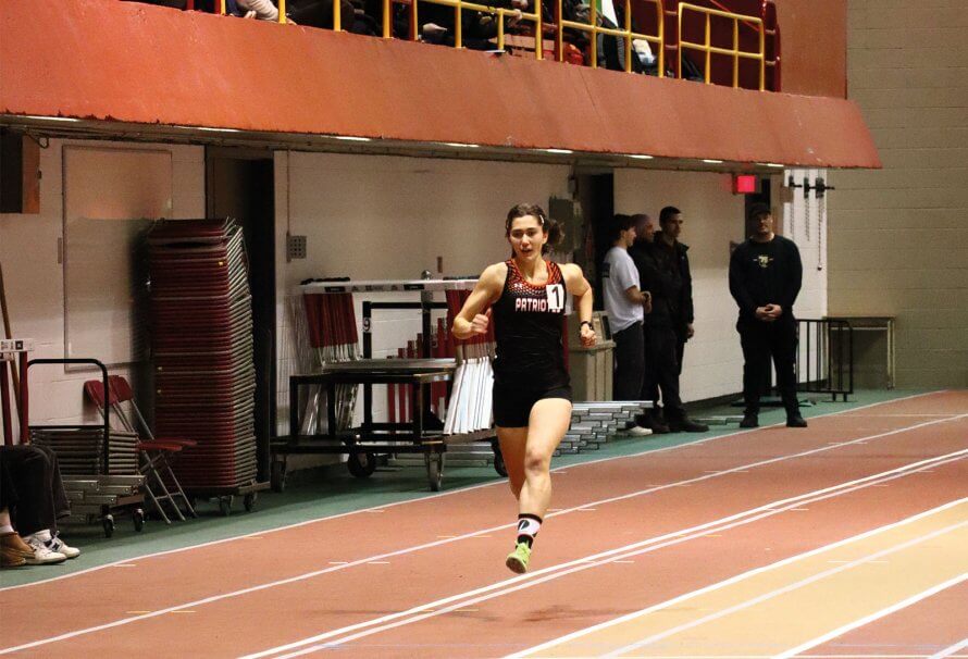 Étudiante-athlète en athlétisme des Patriotes de l'UQTR en plein sprint sur une piste intérieure lors d’une compétition universitaire.