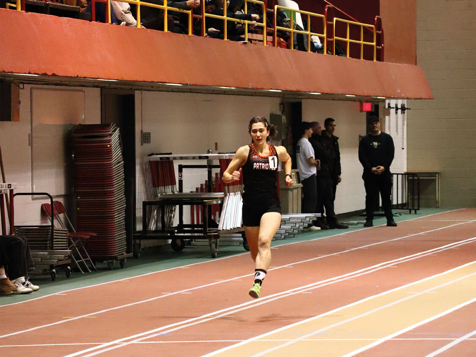 Étudiante-athlète en athlétisme des Patriotes de l'UQTR en plein sprint sur une piste intérieure lors d’une compétition universitaire.