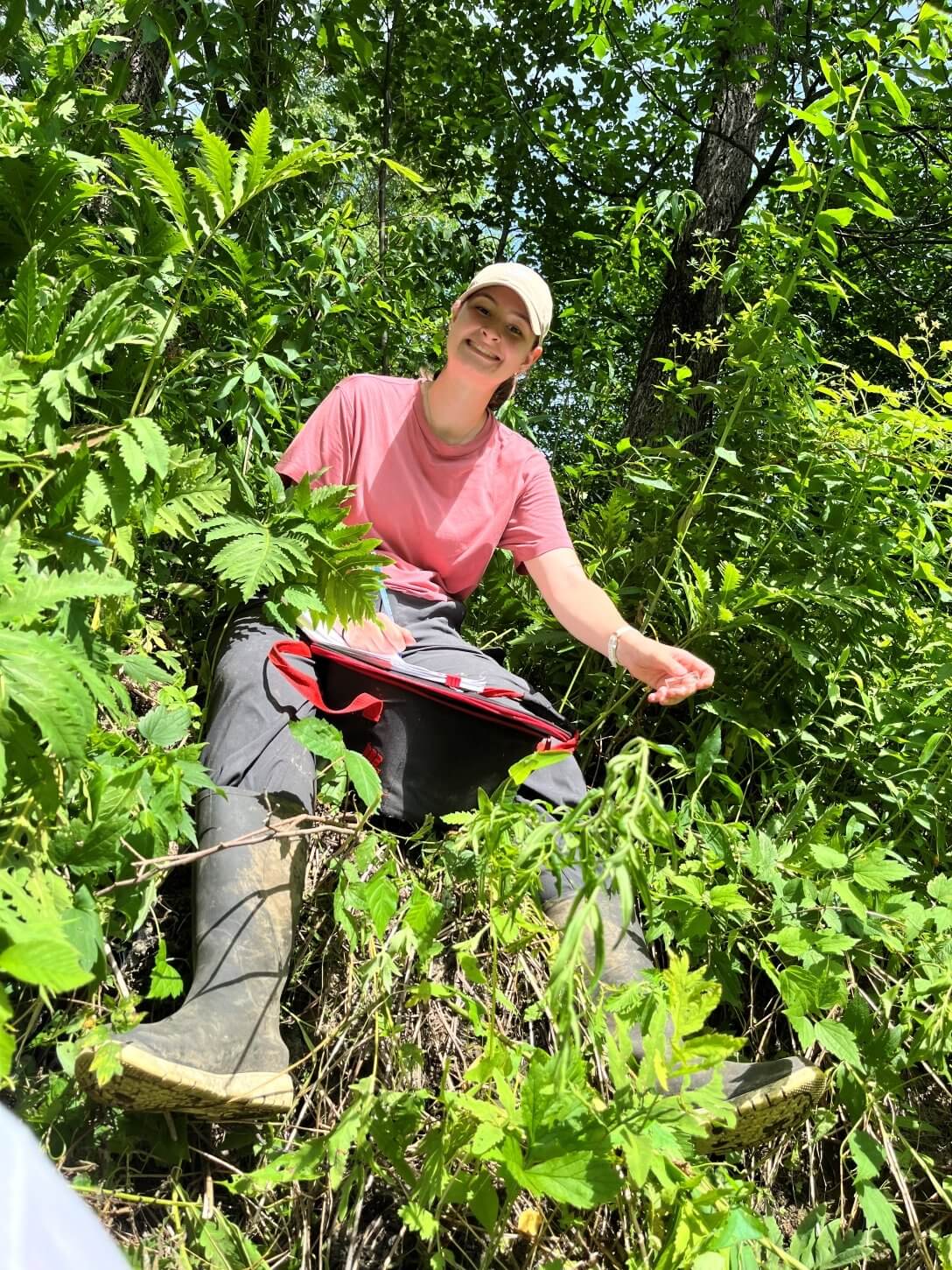 Camille Milot est étudiante à la maîtrise en sciences de l’environnement (profil avec mémoire) de l’UQTR. Elle est ici photographiée sur le terrain, portant de grosses bottes de caoutchouc, et travaillant dans un environnement fortement végétalisé.
