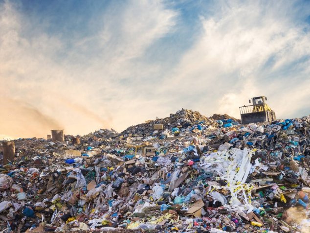 Une montagne de déchets dans une décharge, avec un bulldozer qui entasse les déchets.