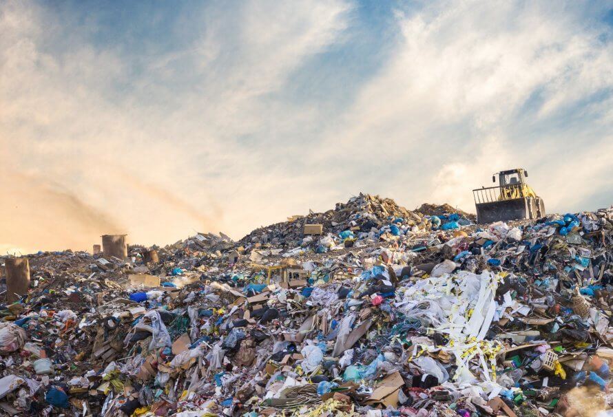 Une montagne de déchets dans une décharge, avec un bulldozer qui entasse les déchets.