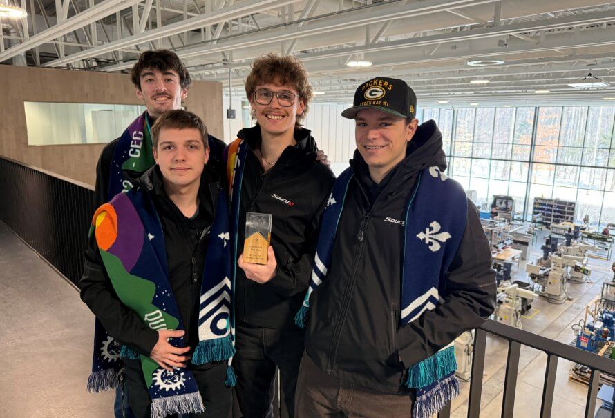 Les quatre membres de l'équipe de Conception sénior du campus de l'UQTR à Drummondville posent ici sur la passerelle du Centre national intégré du manufacturier intelligent (CNIMI), où ils suivent leur formation en génie mécanique. Surplombant l'usine-laboratoire, ils tiennent fièrement leur trophée de deuxième place.