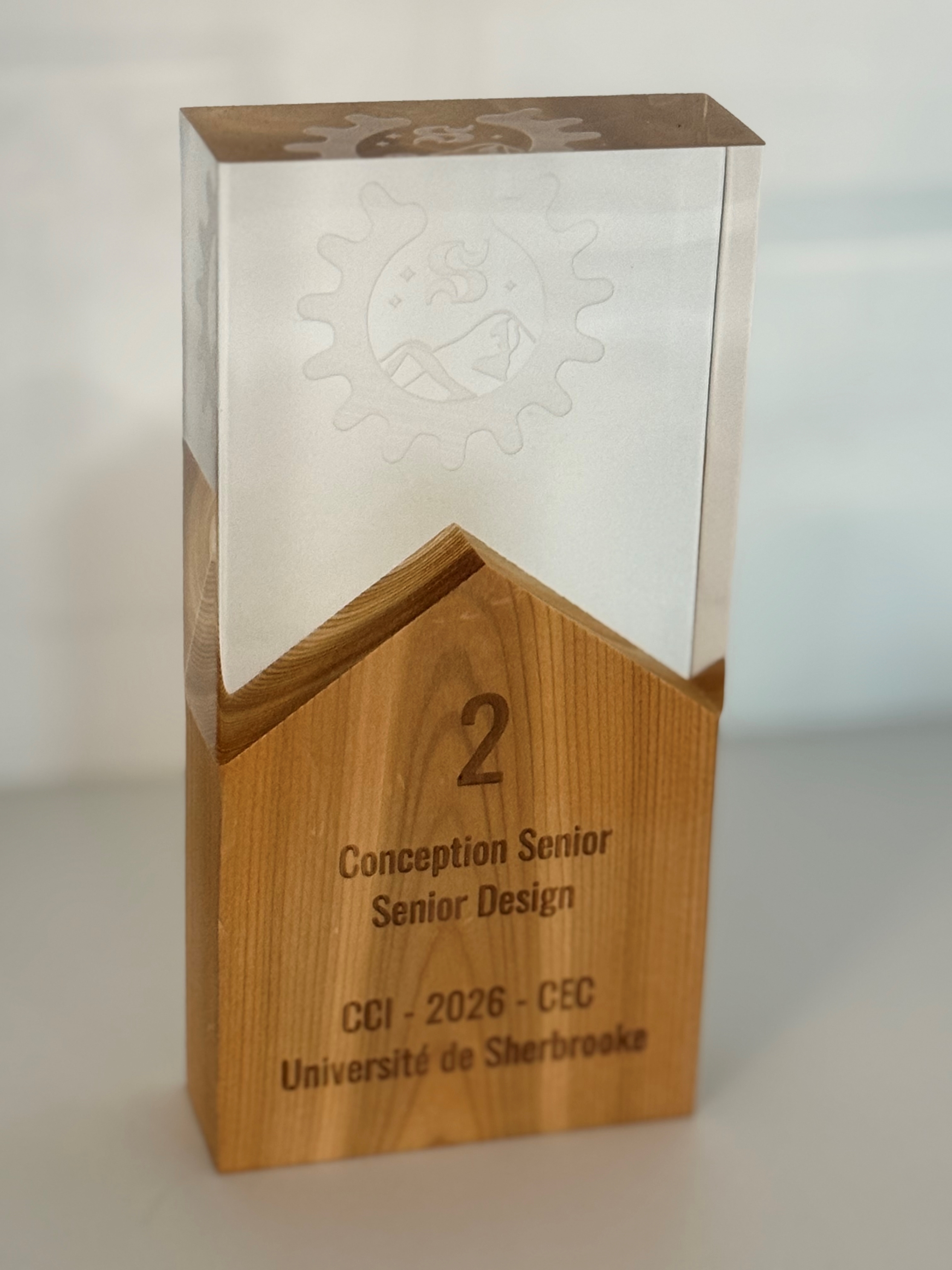 Le trophée remporté par l'équipe de Conception sénior du campus de l'UQTR à Drummondville. La base en bois, sur laquelle on peut lire « 2, Conception sénior / Senior Design, CCI - 2026- CEC, Université de Sherbrooke », est surmontée par un bloc de verre sur lequel est gravé le logo de la compétition.