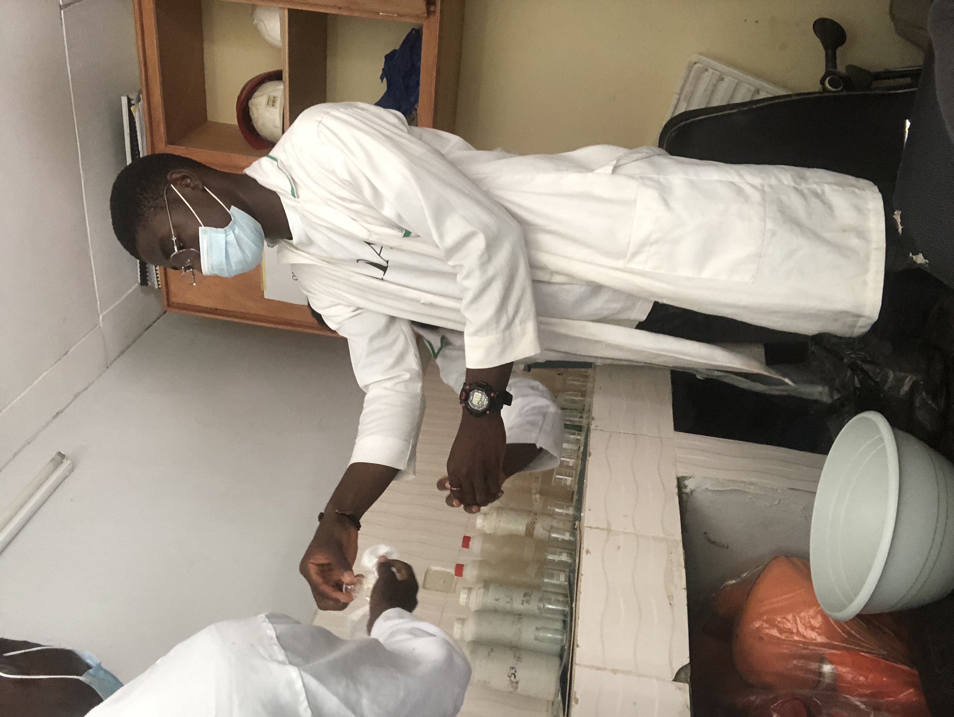 Nanan Romaric Konan est étudiant à la maîtrise en sciences de l’environnement (profil avec mémoire) de l’UQTR. Il est ici photographié en laboratoire, portant un sarrau blanc et un masque chirurgical, et travaillant avec des fioles contenant différents échantillons, en compagnie de collègues.