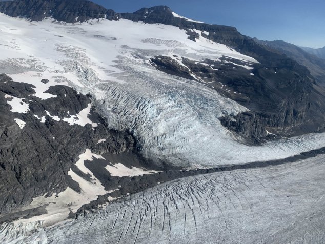 Un glacier situé au cœur d'une région montagneuse. Le contraste entre la roche noire et la glace blanche est saisissant. Une vallée gelée témoigne de l'écoulement des eaux en période de fonte.